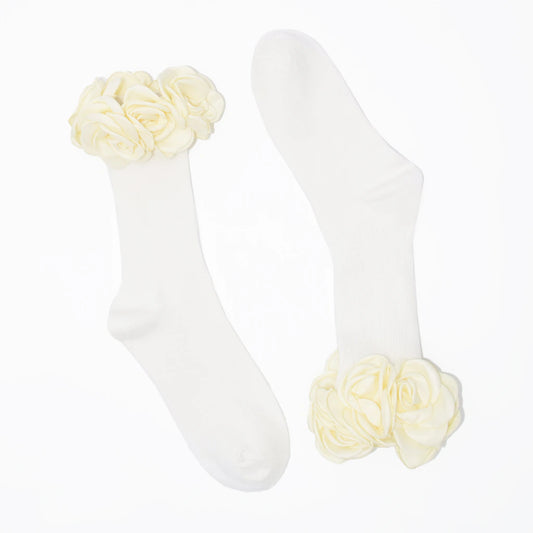 A pair of white crew socks with large cream-colored fabric roses at the top cuff, displayed on a clean white background.