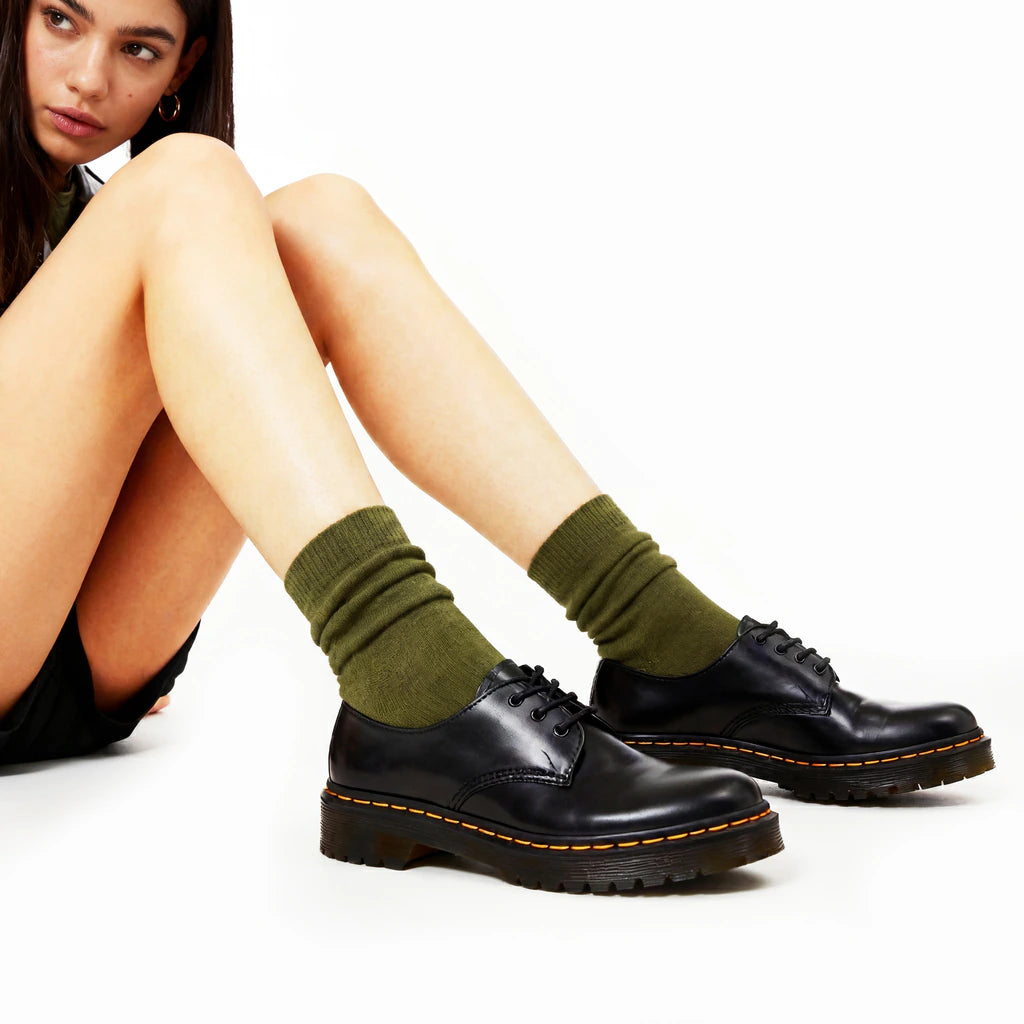 Person wearing green socks and black shoes on a white background