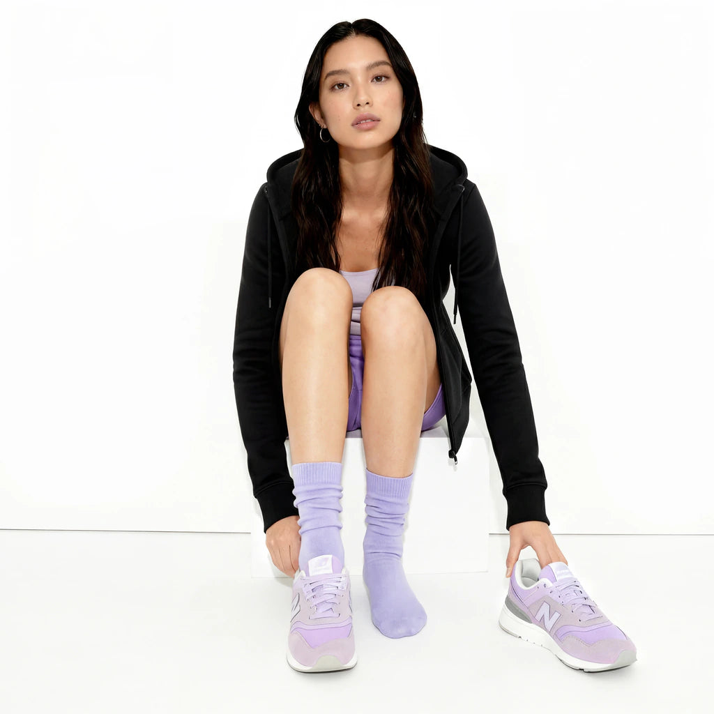 Woman wearing black hoodie, light purple socks, and sneakers on a white background