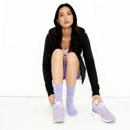 Woman wearing black hoodie, light purple socks, and sneakers on a white background