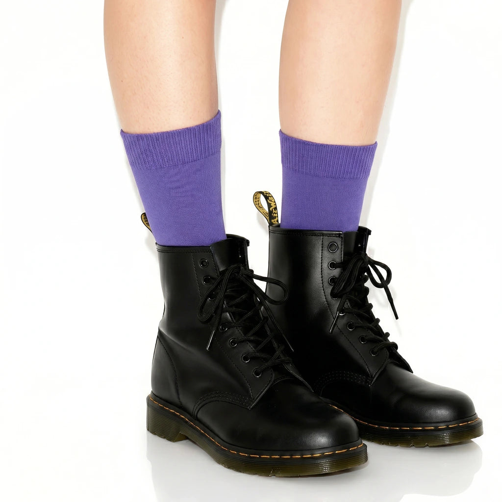 Person wearing black boots and purple socks on a white background