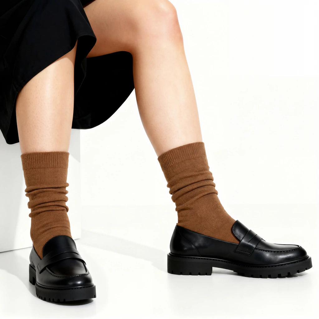 Person wearing brown socks and black loafers on a white background