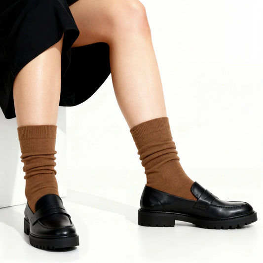 Person wearing brown socks and black loafers on a white background