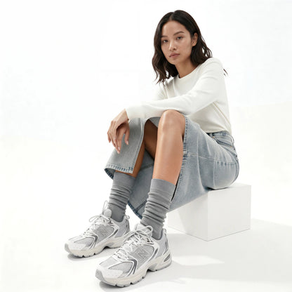 Woman sitting on a white block wearing a white sweatshirt, gray skirt, gray socks, and white sneakers.