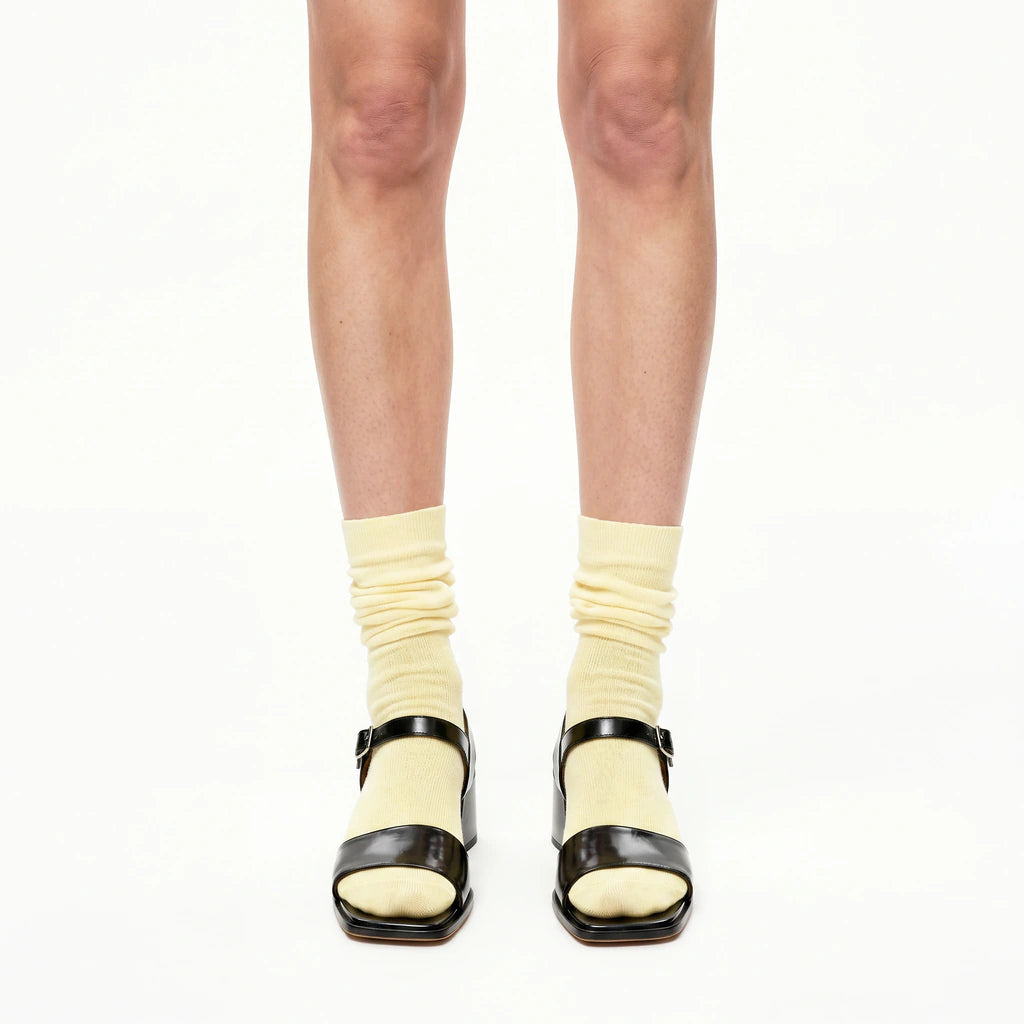 Black block-heel sandals worn with yellow socks on a white background