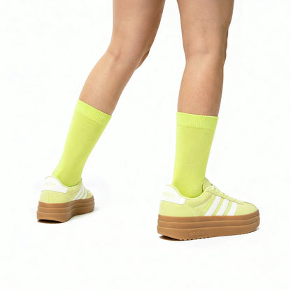 Person wearing bright yellow/green socks and Adidas shoes on a white background