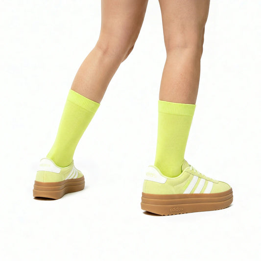 Person wearing bright yellow/green socks and Adidas shoes on a white background