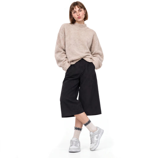 A model wearing a beige fuzzy mock-neck sweater, black wide-leg cropped pants, beige socks, and white sneakers, standing against a plain white background.