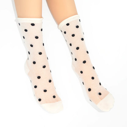 A pair of sheer off-white mesh crew socks with black polka dots, shown on a model's feet against a plain white background.