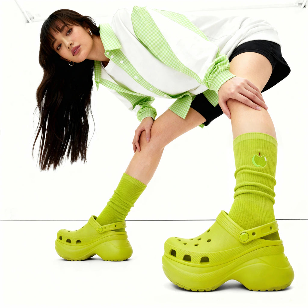 Person wearing lime green platform clogs and socks on a white background