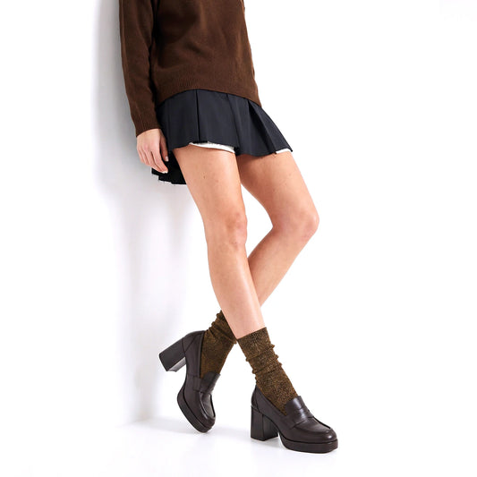 Person wearing a brown sweater, black skirt, and dark shoes with green socks on a white background