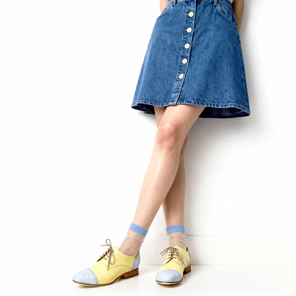 Person wearing a denim skirt, yellow shoes, and light blue socks on a white background