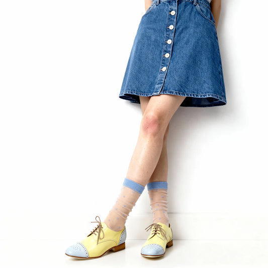 Person wearing a denim skirt, yellow shoes, and light blue socks on a white background