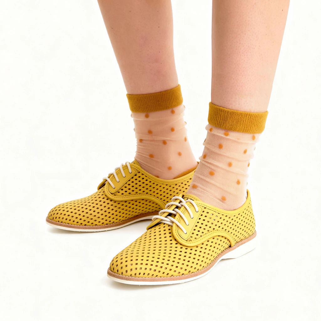 Yellow perforated shoes worn with sheer socks featuring a polka dot pattern on a white background