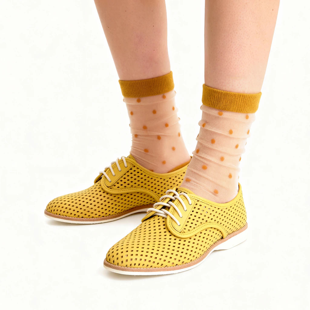 Yellow perforated shoes worn with sheer socks featuring a polka dot pattern on a white background