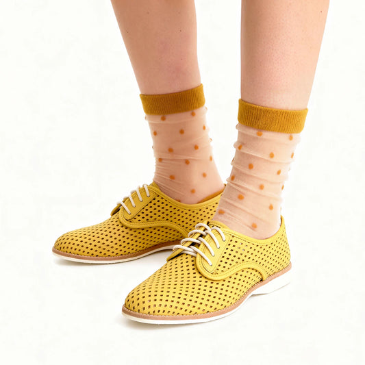 Yellow perforated shoes worn with sheer socks featuring a polka dot pattern on a white background