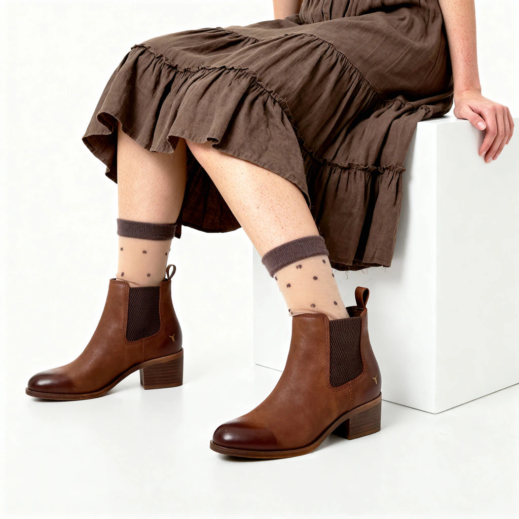Person wearing brown ankle boots and patterned socks sitting on a white block.