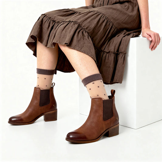 Person wearing brown ankle boots and patterned socks sitting on a white block.