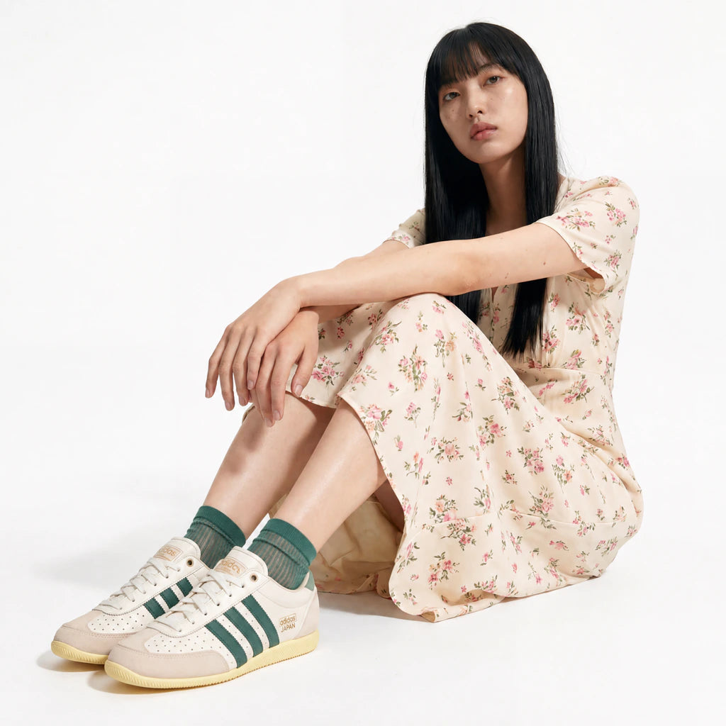 Woman wearing a floral dress and Adidas sneakers sitting on the floor.