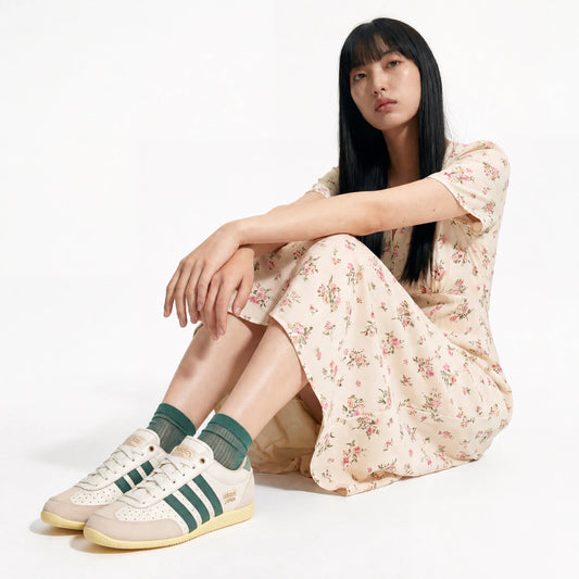 Woman wearing a floral dress and Adidas sneakers sitting on the floor.