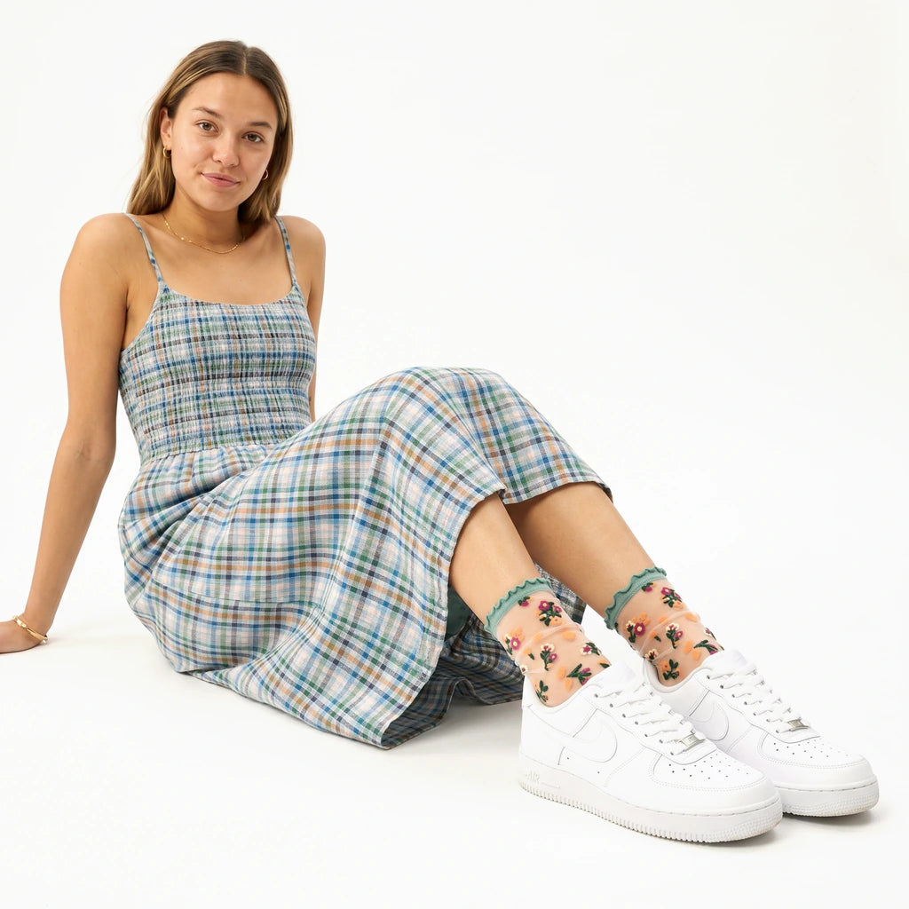 Woman wearing a plaid dress and white sneakers with floral anklets on a white background