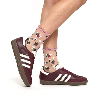Maroon Adidas sneakers with white stripes worn with floral sheer socks on a white background