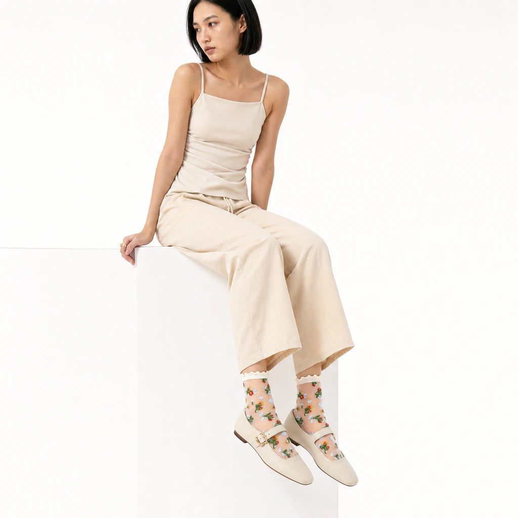 Woman wearing a beige dress and floral socks sitting on a white background