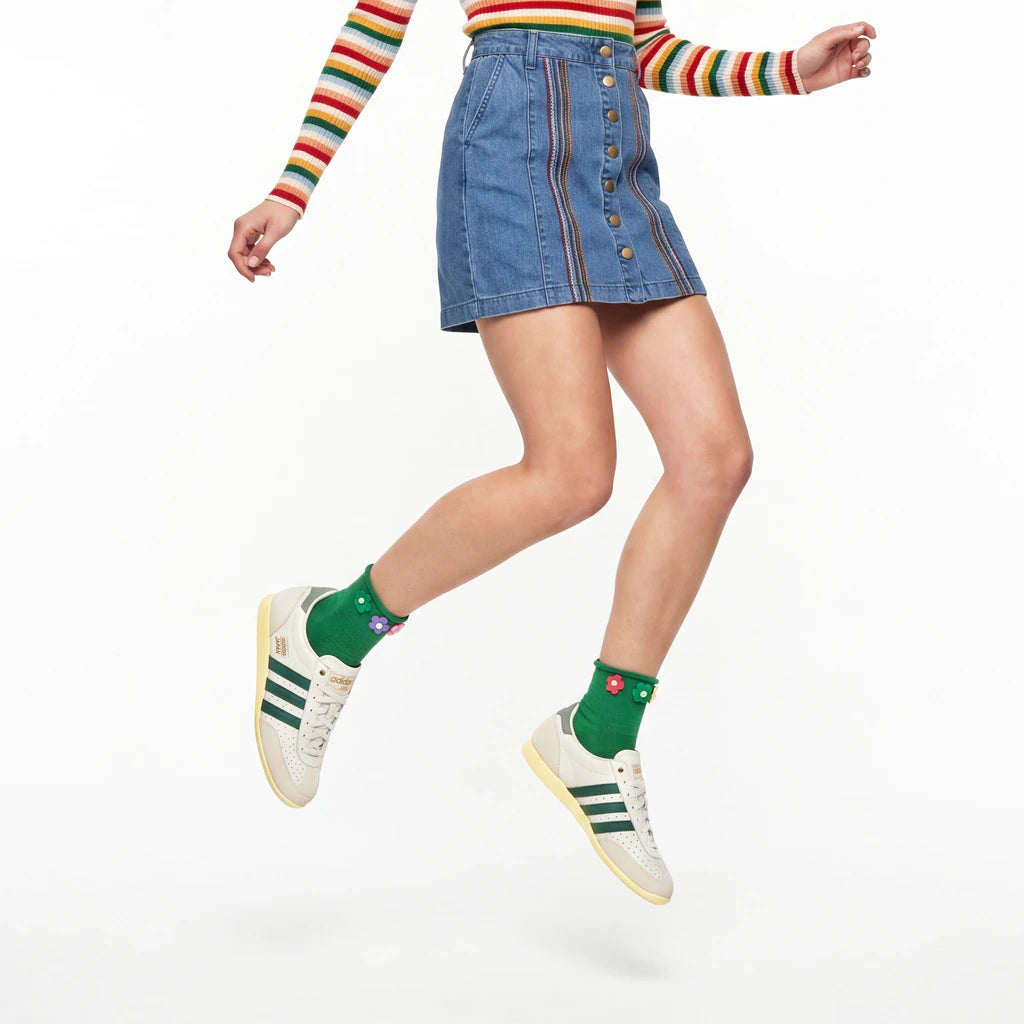 Person wearing a rainbow striped sweater, denim skirt, green socks, and white sneakers on a white background