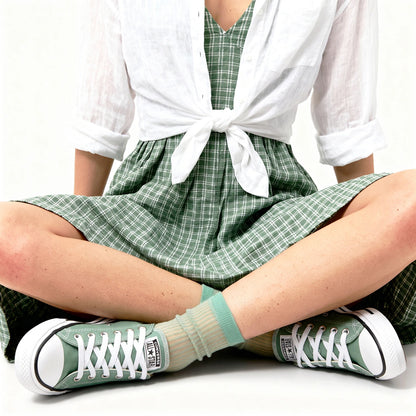 Person wearing green checkered dress, white shirt, and green sneakers with beige socks.
