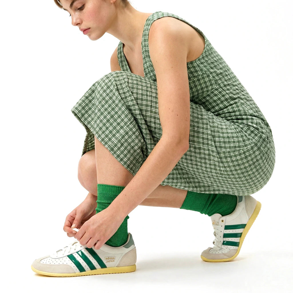 Person wearing green checkered dress and Adidas shoes on a white background