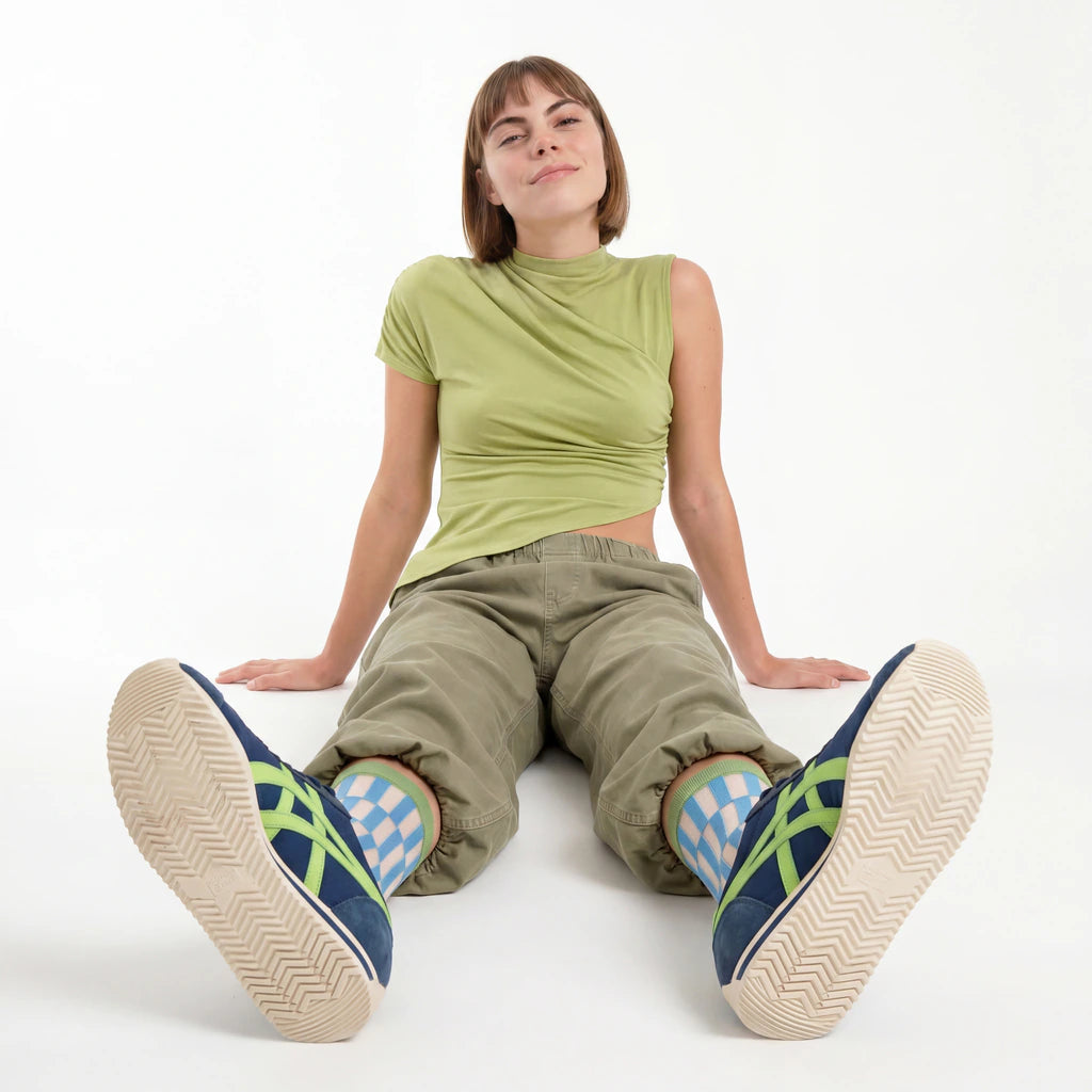 Person wearing green shirt and beige pants with blue and green shoes on a white background
