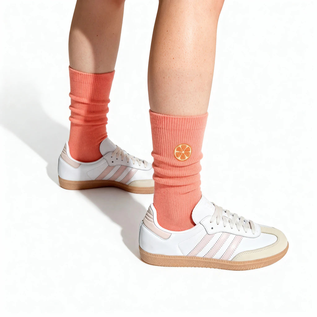 Person wearing coral socks with a grapefruit motif and white sneakers on a white background
