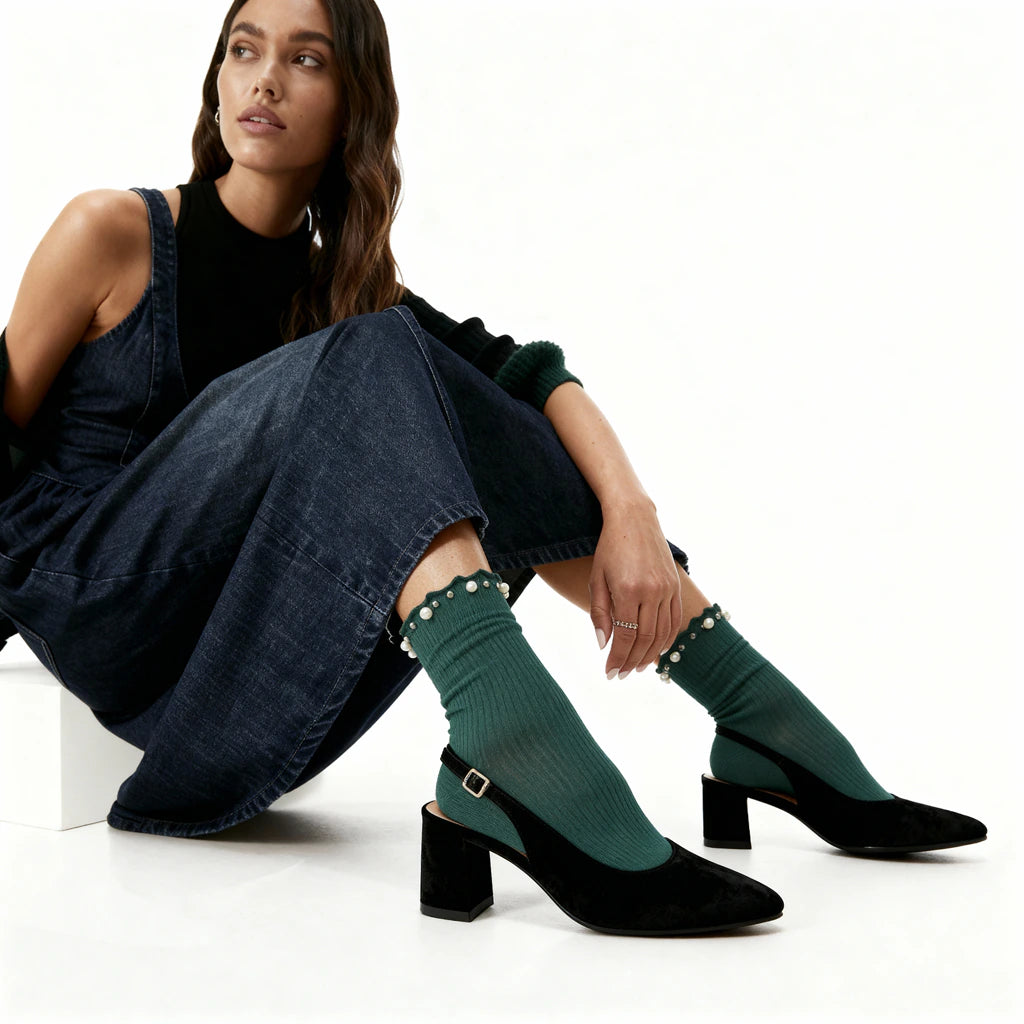 Woman wearing green socks with decorative elements and black high-heeled shoes on a white background