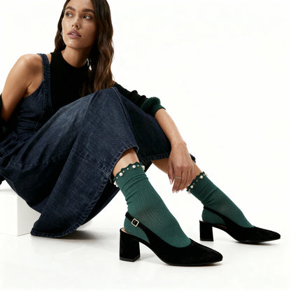 Woman wearing green socks with decorative elements and black high-heeled shoes on a white background