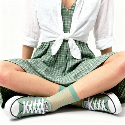 Person wearing green checkered dress, white shirt, and green sneakers with beige socks.