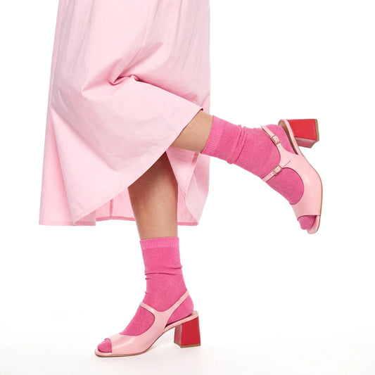 Pink high-heeled shoes and socks worn with a pink skirt on a white background