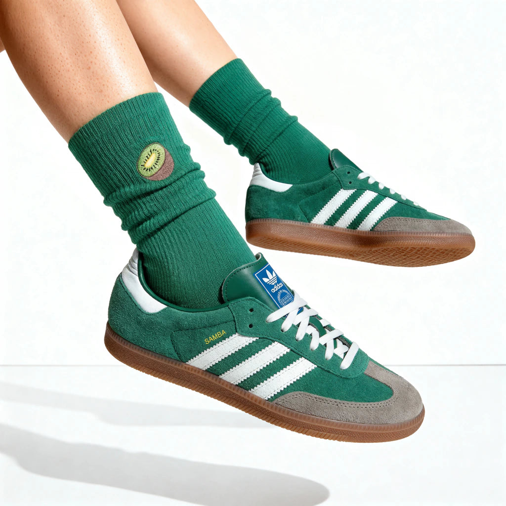 Green Adidas sneakers with white stripes worn by a person on a white background