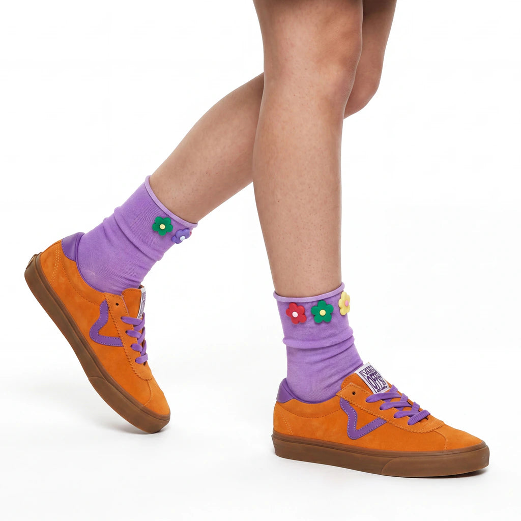 Orange sneakers with purple laces and socks featuring colorful flowers on a white background