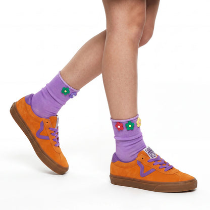 Orange sneakers with purple laces and socks featuring colorful flowers on a white background