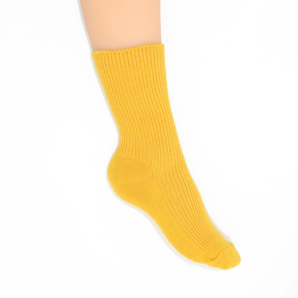 A single ribbed ankle sock in a bright golden yellow color, shown on a  leg against a plain white background.
