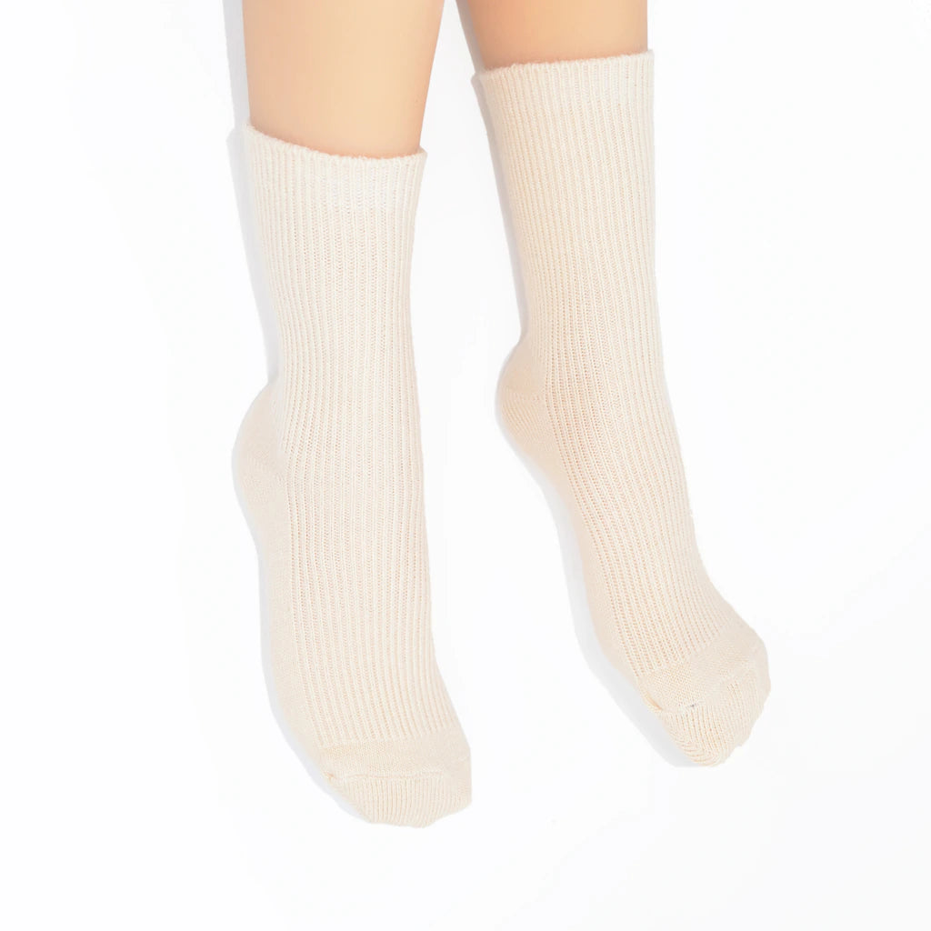 A pair of ribbed ankle socks in a light cream or off-white color, shown on  legs against a plain white background.