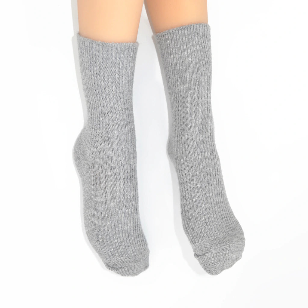 A pair of light gray ribbed crew socks worn on legs against a plain white background.