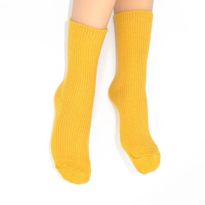 A pair of ribbed ankle socks in a solid mustard yellow color, shown on a person's feet against a plain white background.