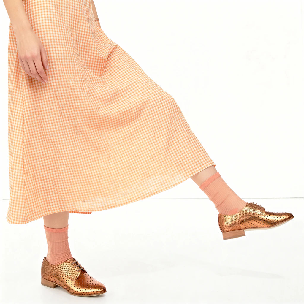 Person wearing a checkered dress and gold shoes on a white background