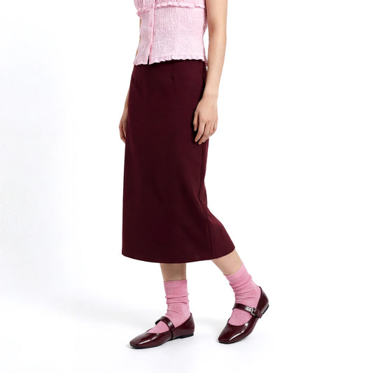 Person wearing a pink top, maroon skirt, and pink shoes on a white background