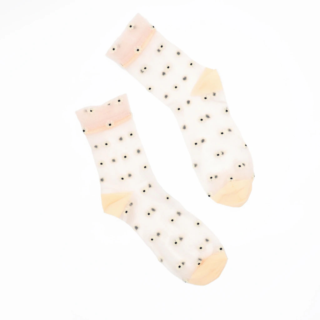 A pair of sheer white ankle socks with small black polka dots and soft peach-colored toe and cuff accents, displayed on a clean white background.