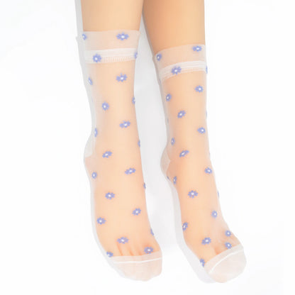 A pair of sheer white ankle socks with a small blue and white floral pattern, shown on a leg against a white background.