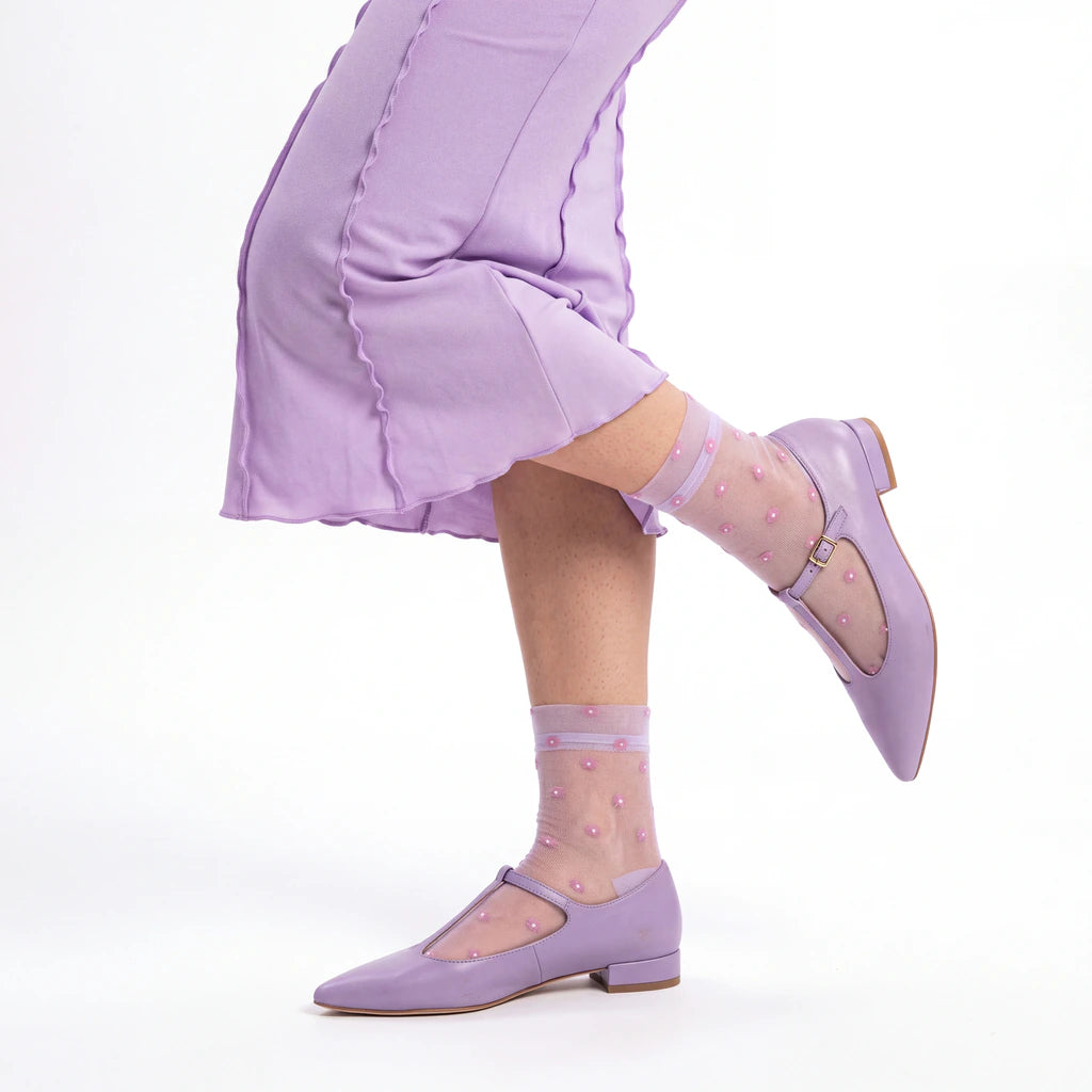 A person wearing light purple Mary Jane shoes and sheer light purple socks with pink polka dots, paired with a matching light purple skirt, shown against a plain white background.