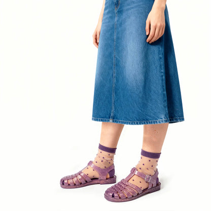 Person wearing purple sandals and socks with a blue denim skirt on a white background