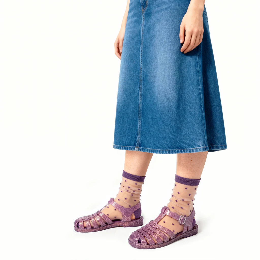 Person wearing purple sandals and socks with a blue denim skirt on a white background